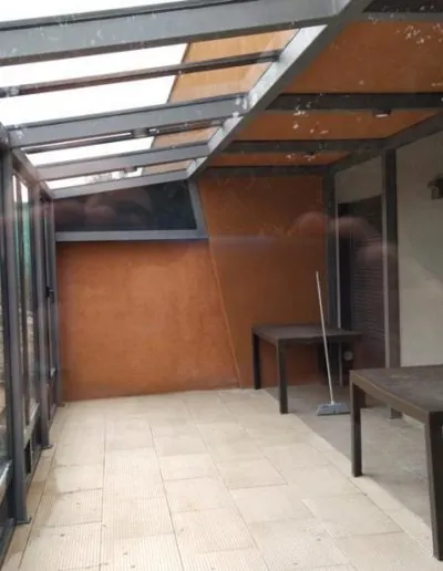 Porche acristalado con techo, junto a una pared de barro