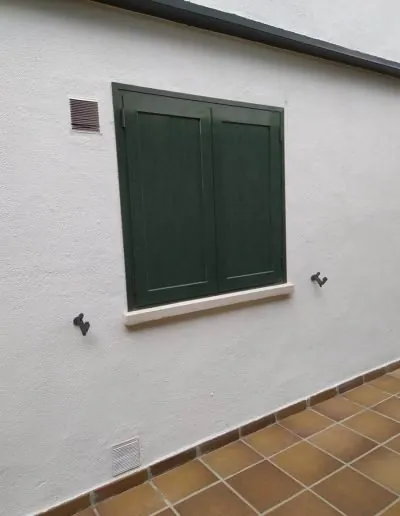 Ventana de aluminio con contraventana verde en una fachada blanca