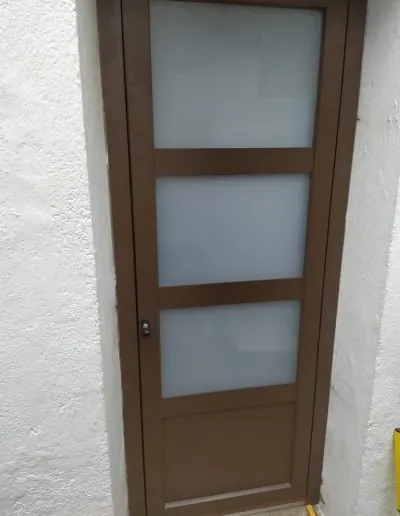 Puerta marrón con cristales traslúcidos en una fachada blanca