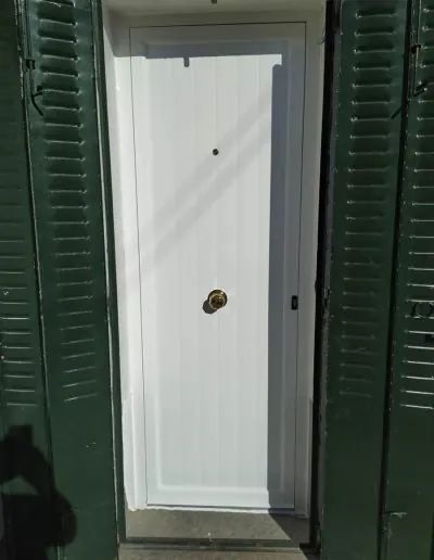 Puerta blanca de PVC entre contraventanas verdes