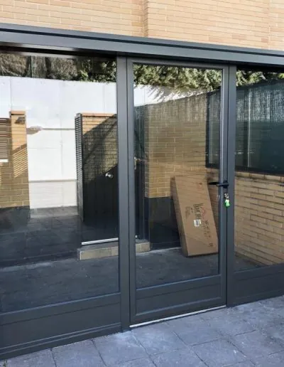 Puerta de aluminio gris de doble hoja en un acceso peatonal