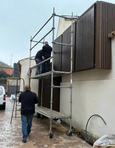 Dos operarios instalando un cerramiento de lamas en una fachada